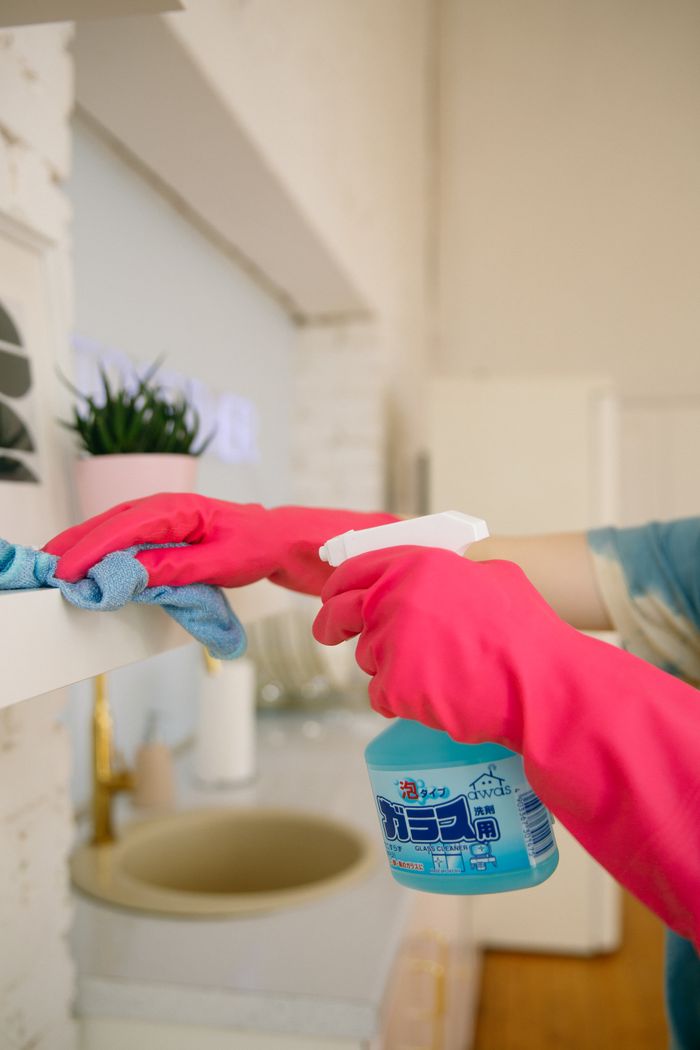 about-us-01 A person cleaning a kitchen shelf with a spray bottle and cloth, keeping it hygienic and spotless.